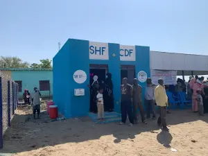 أشخاص ينتظرون أمام مبنى أزرق جديد لمساحة صديقة للأطفال يحمل اسم المنظمة وصندوق مانح
