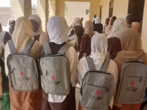تلميذات يقفن في ممر المدرسة وعلى ظهورهن حقائب جديدة تحمل شعار المنظمة وشعار الجهة الشريكة