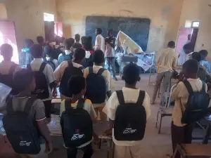 تلاميذ داخل فصل دراسي يحملون حقائب جديدة بينما يقف موظفان عند السبورة