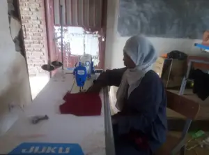 امرأة تعمل على ماكينة خياطة أمام قطعة قماش حمراء في قاعة تدريب مهني